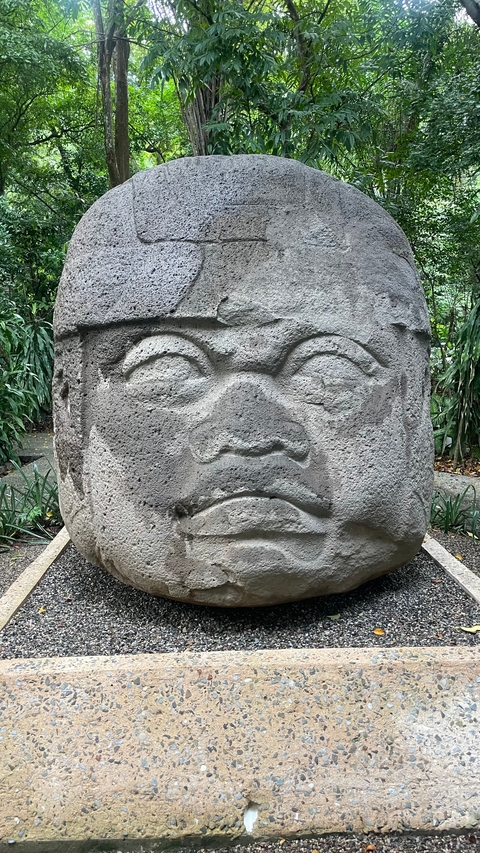       A large stone head sculpture in a garden setting.
  