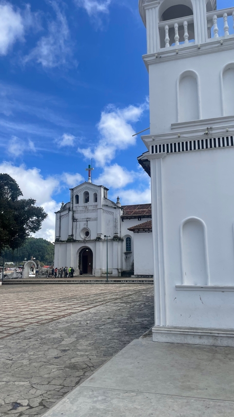       White church buildings with a cross against a blue sky.
  