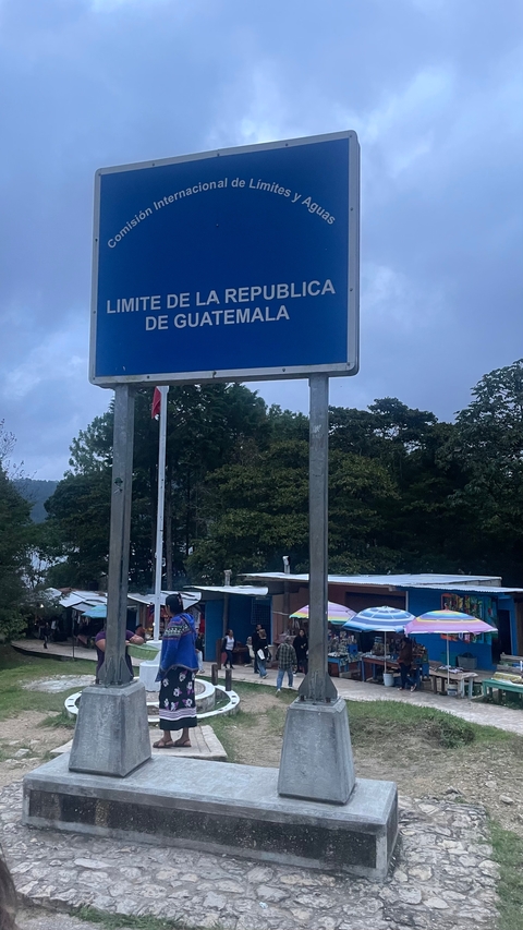       A blue sign at a roadside, with forested hills in the background.
  
