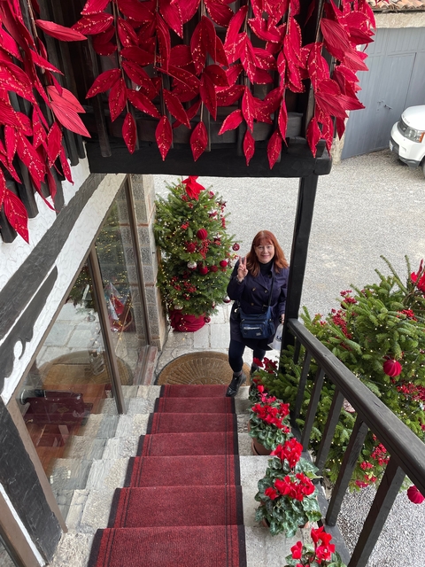 A woman posing by decorated Christmas trees outside a building.