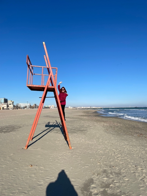 Person posing on a lifeguard stand at a beach.