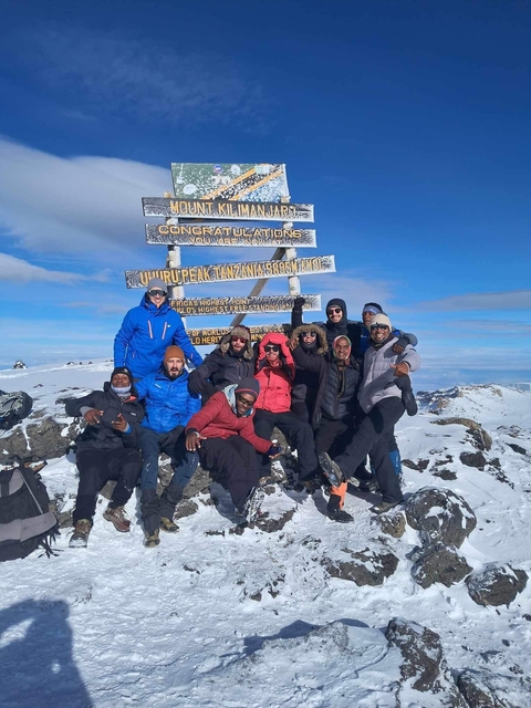       A group of people posing on a snowy mountain summit with a sign reading 'Uhuru Peak'.
  