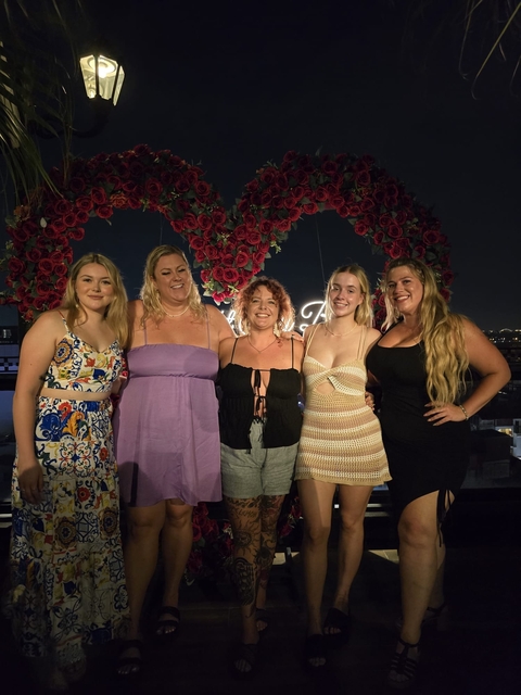 A group of women smiling and standing in front of a floral backdrop.