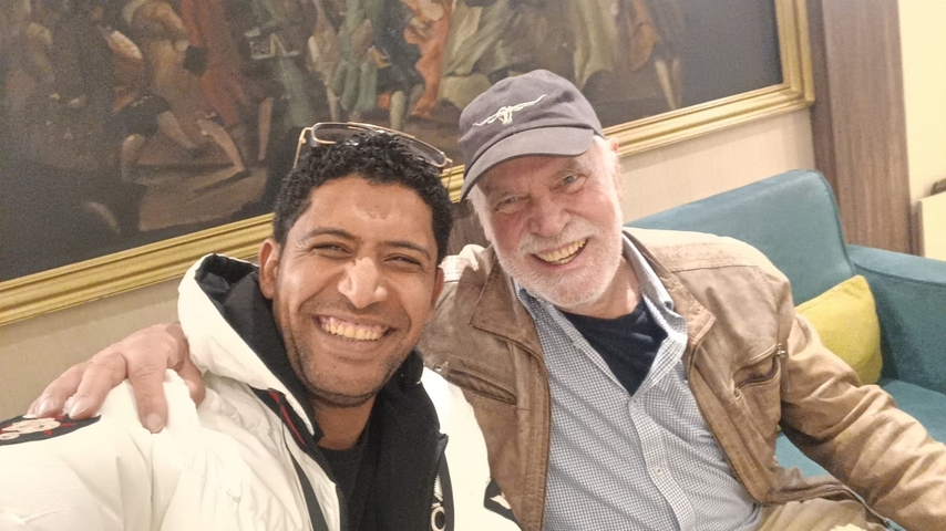 Two people smiling indoors with artwork in the background.