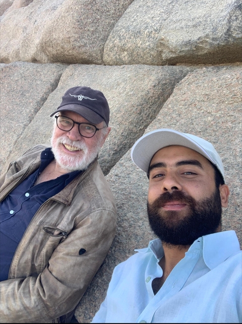 Two men smiling at the camera with ancient stone backdrop.