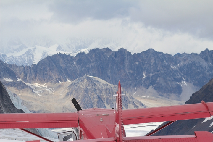       A scenic view of mountains with a small red plane parked in the front.
  