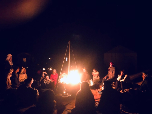 Group of people sitting around a campfire at night.