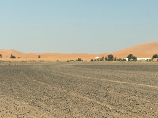 Desert landscape with scattered trees and tents.