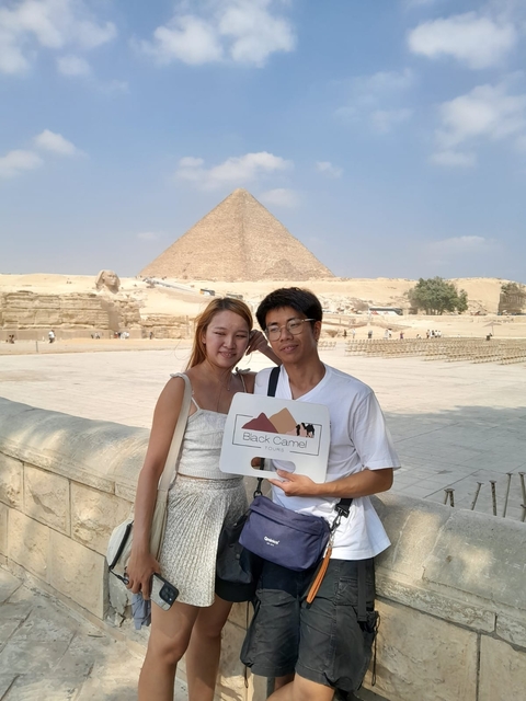       Two people posing with a view of the Giza pyramids.
  
