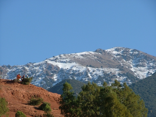 Two people sitting on a hill with snow-capped mountains.