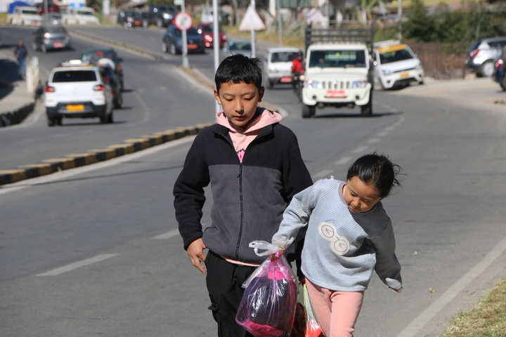       Two children walking on a street with traffic.
  