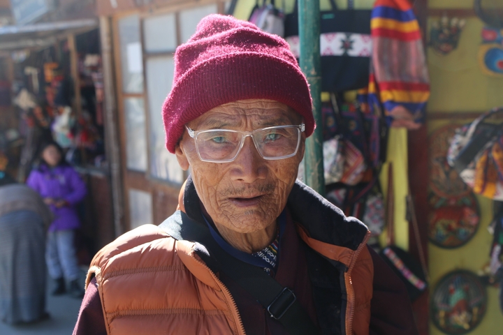       Elderly person wearing glasses with market surroundings.
  
