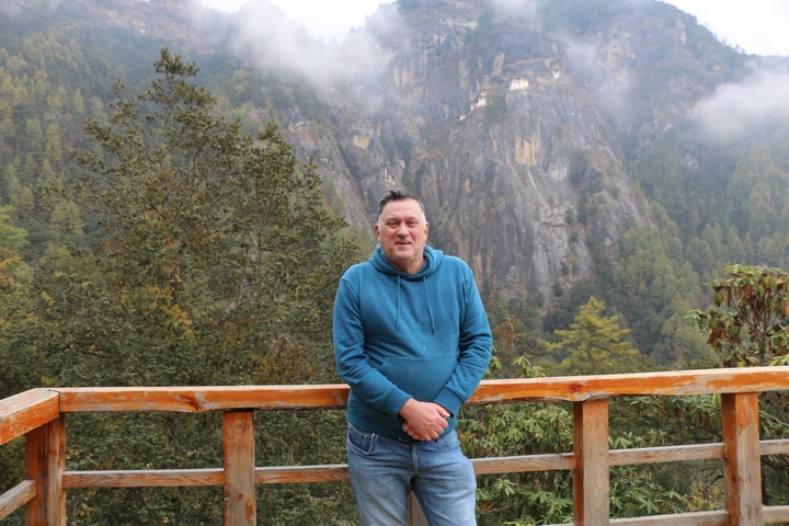       Person standing on a wooden balcony with a mountainous view.
  