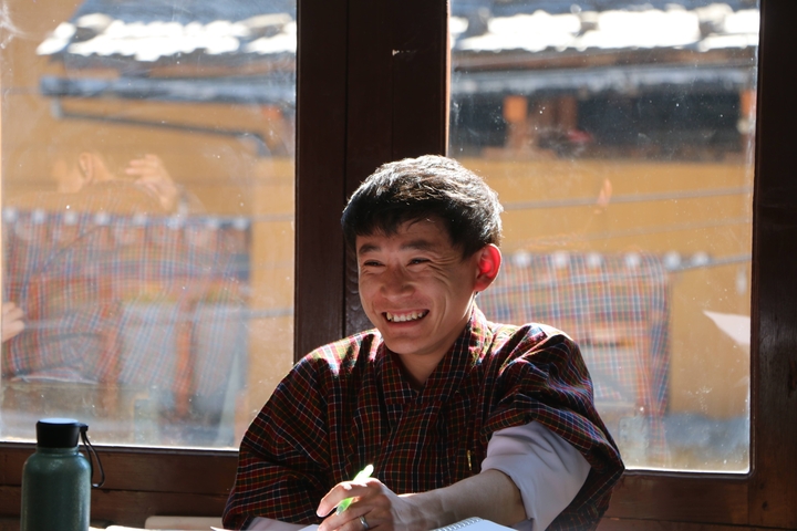       Person smiling indoors with Bhutanese houses in the background.
  
