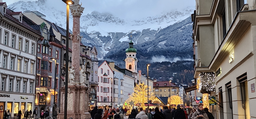       Crowded street with festive decorations and mountains in background.
  