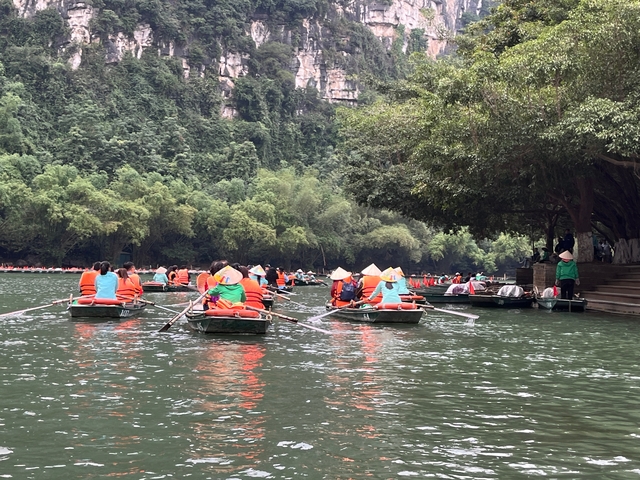       People rowing boats wearing colorful jackets and hats on a lush green river.
  