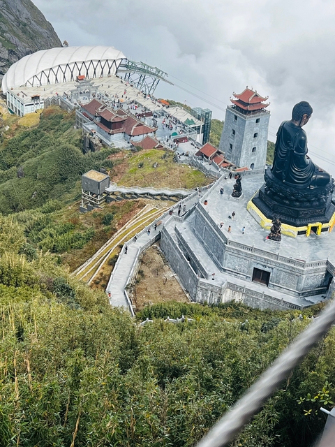 A view from above of tourists and a large statue at a mountainous area with a staircase.