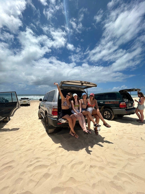 Four women sitting on the back of a parked SUV on a sandy beach.