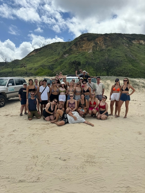       A large group of people posing on a sandy beach in front of SUVs.
  