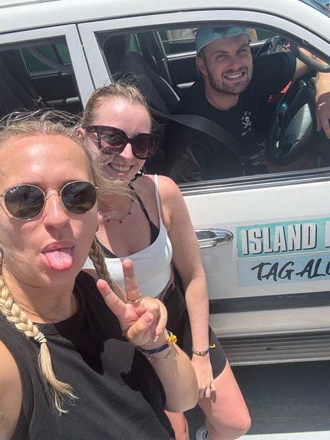 Two women smiling and posing beside a vehicle with a sign that reads 'Island Tag'.