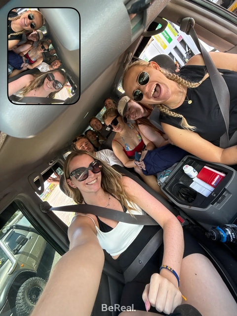       A group of people smiling inside a vehicle, taking a selfie.
  