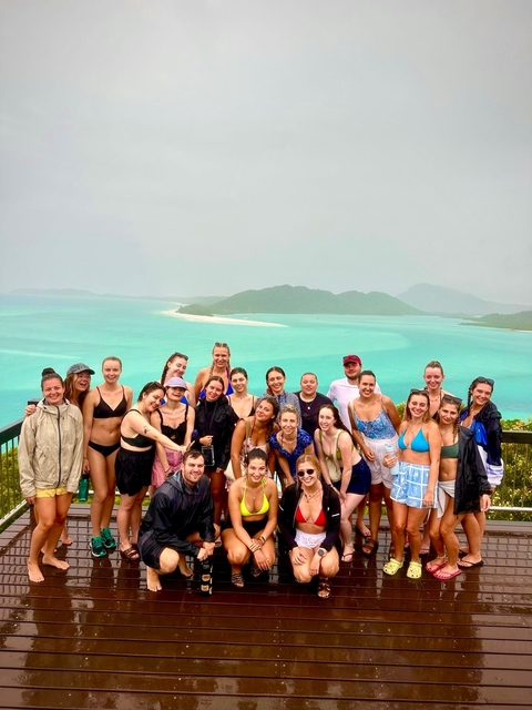       A large group posing with a view of turquoise waters, likely on an island.
  