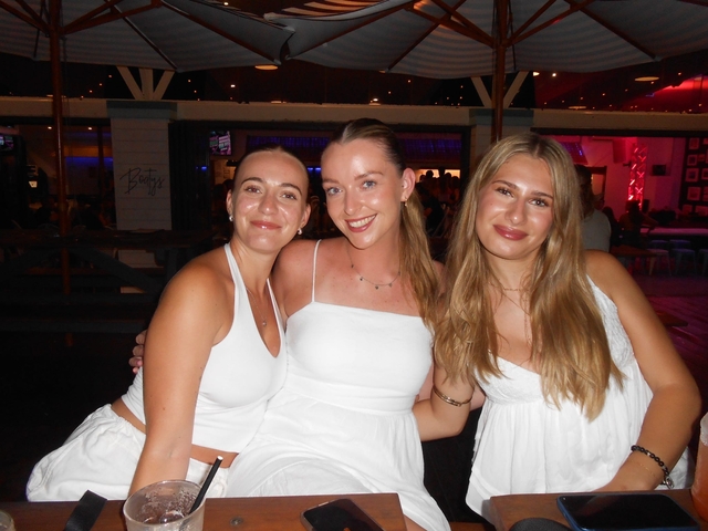       Three women sitting together indoors, dressed in white clothing.
  