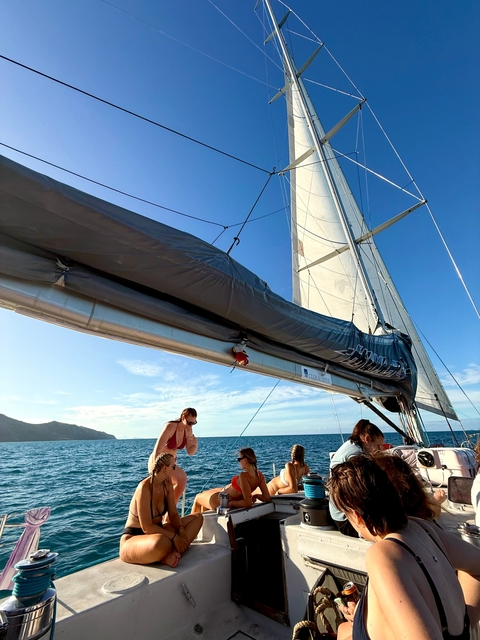       A person on a sailing boat with sails, enjoying the view of the ocean.
  