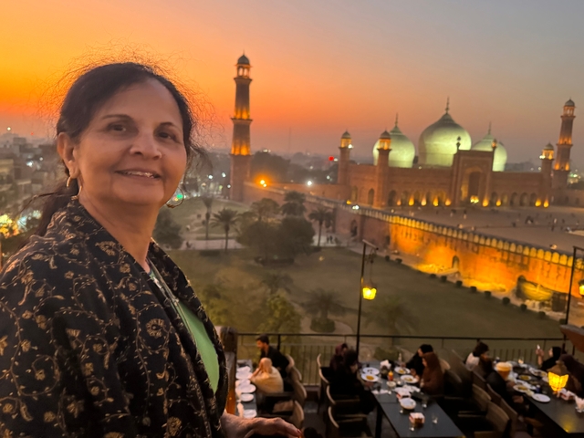 A person smiling with the Badshahi Mosque in the background during sunset.