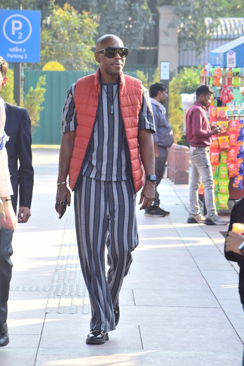       Man in striped outfit walking in a busy area.
  