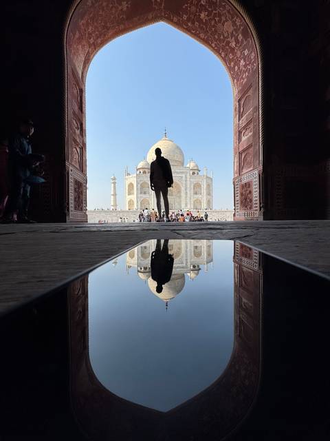       Reflection of Taj Mahal in a pool with a silhouette.
  