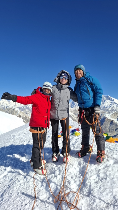       Three climbers in winter gear stand on a snow-capped mountain peak.
  