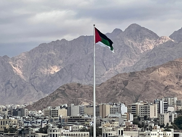       A flag of Jordan with mountains in the background.
  