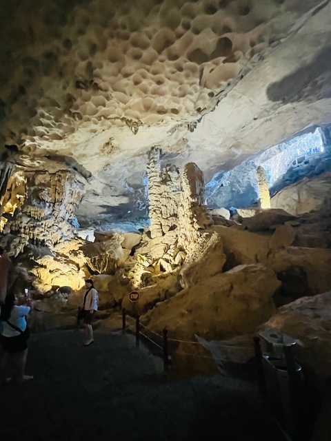       Tourist exploring a lit cave with stalactites and stalagmites.
  