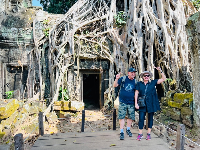       Tourists posing in front of a temple engulfed by tree roots.
  