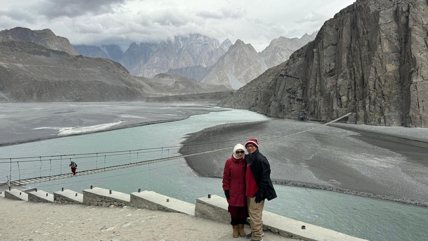 Couple posing in front of a scenic mountain river with a suspension bridge.