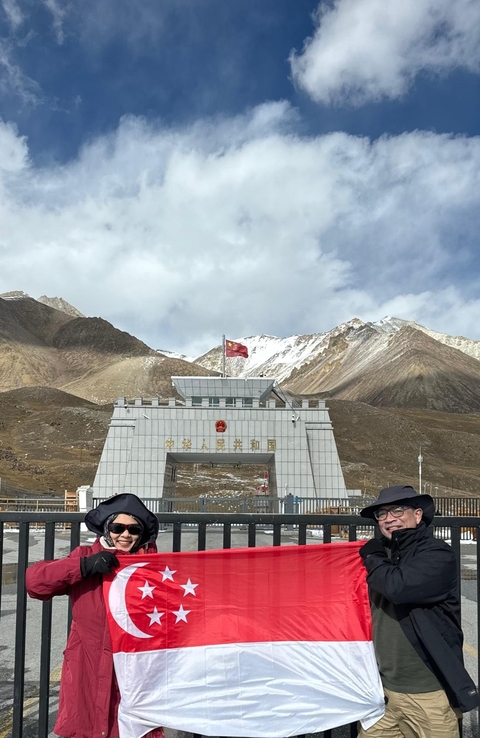 People standing in front of the border gate with mountains in the background.