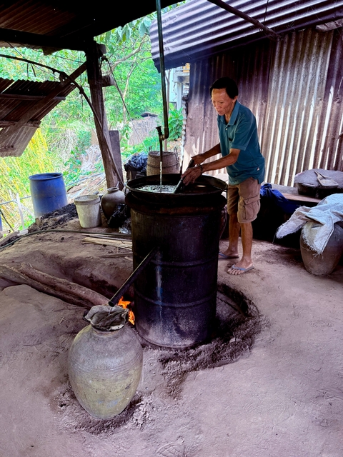       Person working in a rustic setting with large pots and a flame.
  