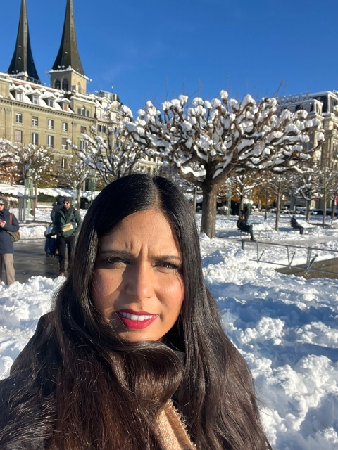 Person posing in a snowy urban park with trees in the background.