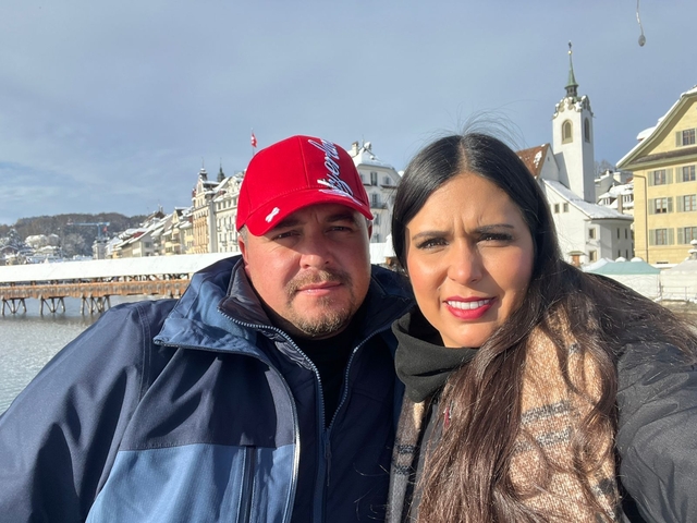 Two people posed in front of a snowy cityscape with a bridge.