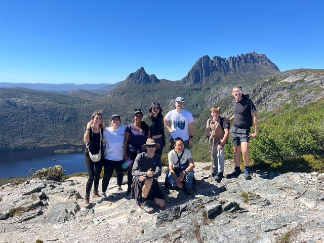       Group of hikers posing on a mountain top with stunning views.
  