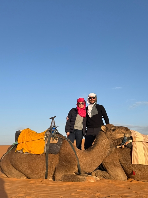       Couple standing with camels in a desert landscape.
  