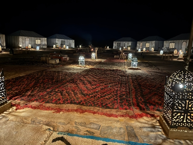       Night view of a desert camp with lanterns and Moroccan rugs.
  