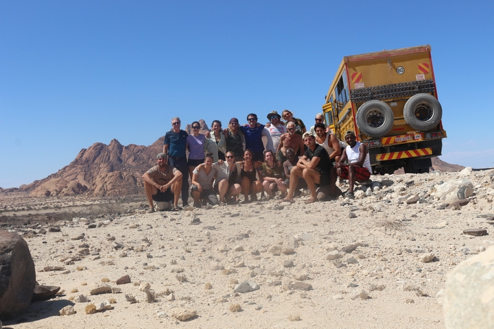 Group of people posing with a safari truck in a desert landscape.