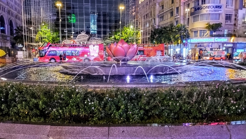 Illuminated fountain with a red lotus shape at night in a city square.