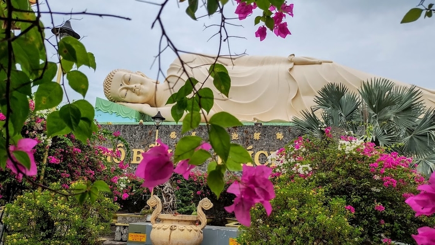       Reclining Buddha statue surrounded by flowers and greenery.
  