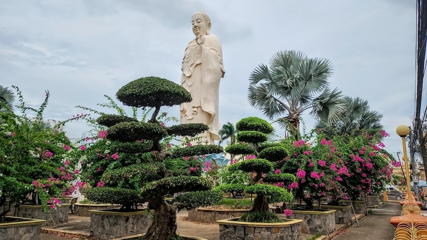 Standing Buddha statue with manicured gardens and flowering plants.