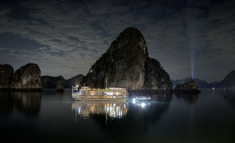 Night view of illuminated boat on the water against a backdrop of limestone karsts.
