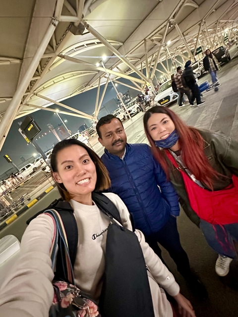       Three people posing at a busy airport entrance.
  