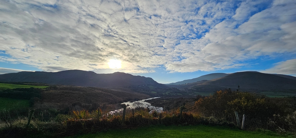 Landscape view with sun setting over mountains and river.